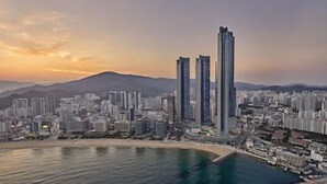 A coastal cityscape with modern high-rise buildings, a beach, and mountains in the background. - Signiel Busan (Busan)