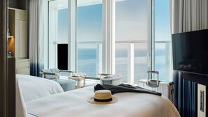 A hotel room with a large window, a bed, a TV, and a seating area with a view of the sea. - Signiel Busan (Busan)