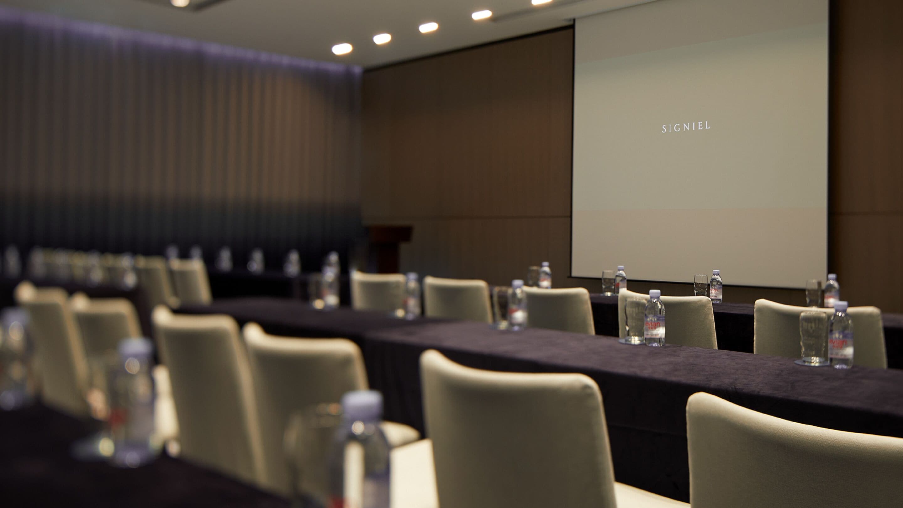 A conference room with a long table, chairs, and a projector screen displaying "SIGNIEL".
