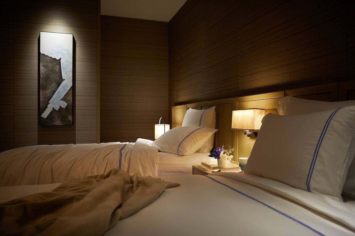 A hotel room with a large bed, bedside tables, a wall-mounted artwork, and a nightstand with a lamp.
