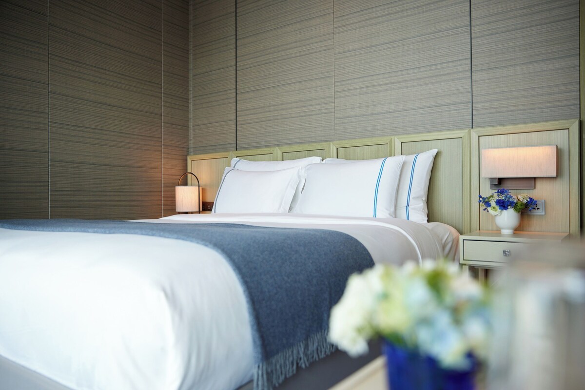 A hotel room with a large bed, a nightstand with a lamp, and a wall-mounted light fixture.