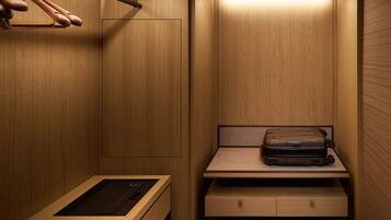 A compact, well-lit walk-in closet with wooden walls, a hanging rack, a bench with drawers, and a suitcase on the bench.