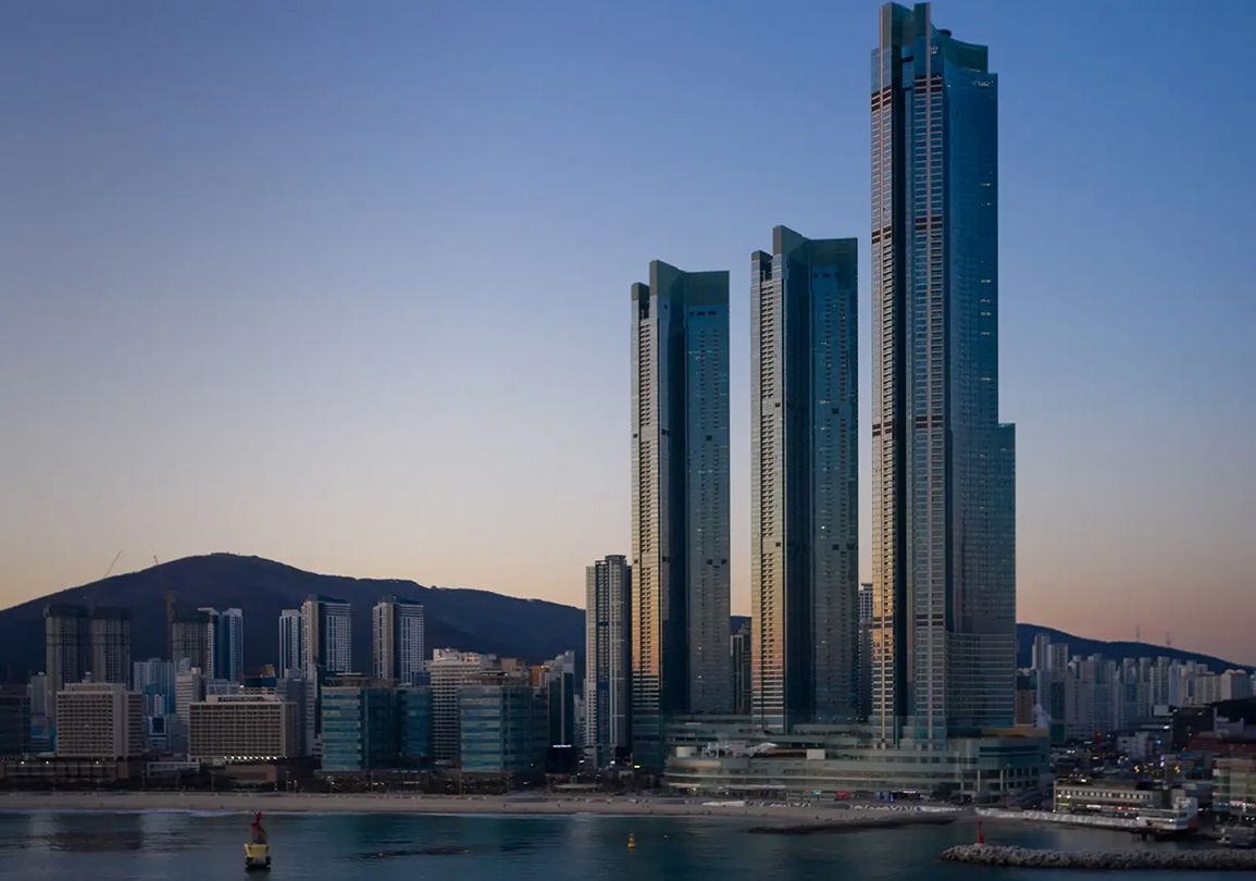 A cityscape with modern high-rise buildings, a body of water, and a mountain in the background.