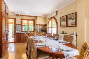 Un coin repas avec une table en bois dressée pour six personnes, entourée de chaises en osier, et une cuisine en arrière-plan.