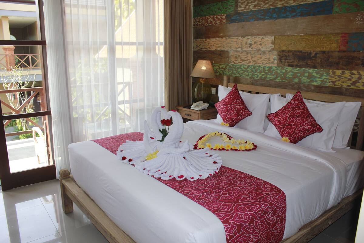 A neatly made bed with a red and white patterned bedspread, white pillows, and a floral arrangement on the side.