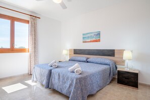 Een slaapkamer met twee bedden, een nachtkastje met een lamp, een schilderij aan de muur en een raam met gordijnen.