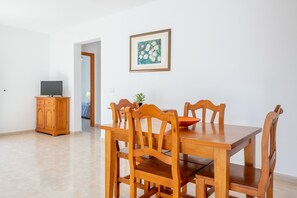 Een eethoek met een houten tafel en stoelen, een televisie op een kast en een lijst met een afbeelding aan de muur.