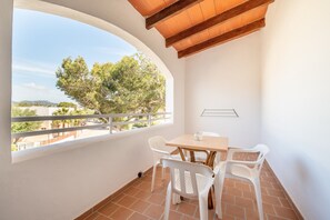 A balcony with a table and chairs, a view of trees and buildings, and a tiled floor.