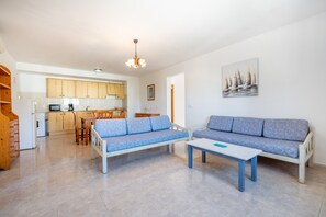 A living room with two blue sofas, a white coffee table, and a kitchen in the background.