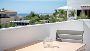 A balcony with a table and a glass jar, overlooking a coastal area with buildings and greenery. - Air-conditioned Apartment with Pool, Wi-Fi, Balcony, and Close to the Beach (Cala D'or)