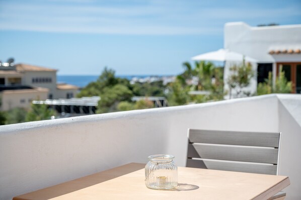 A balcony with a table and a glass jar, overlooking a coastal area with buildings and greenery. - Apartment with Air Conditioning, Pool, Wi-Fi and Balcony near the Beach (Cala D'or)