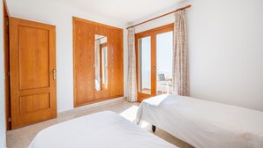 A hotel room with two beds, wooden doors, a balcony with a chair, and a view. - Air-conditioned Apartment with Pool, Wi-Fi, Balcony, and Close to the Beach (Cala D'or)