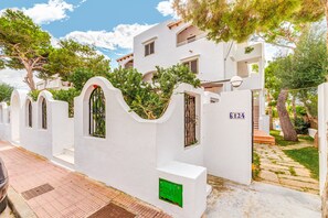 Un bâtiment blanc doté de balcons, une allée pavée et un chemin bordé d’arbres.