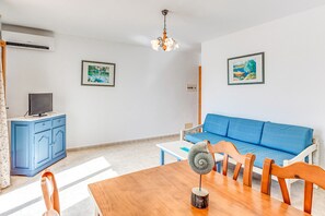 Ein Wohnzimmer mit blauem Sofa, Esstisch aus Holz und Deckenventilator.