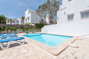 A swimming pool with lounge chairs, white buildings, and a clear sky.