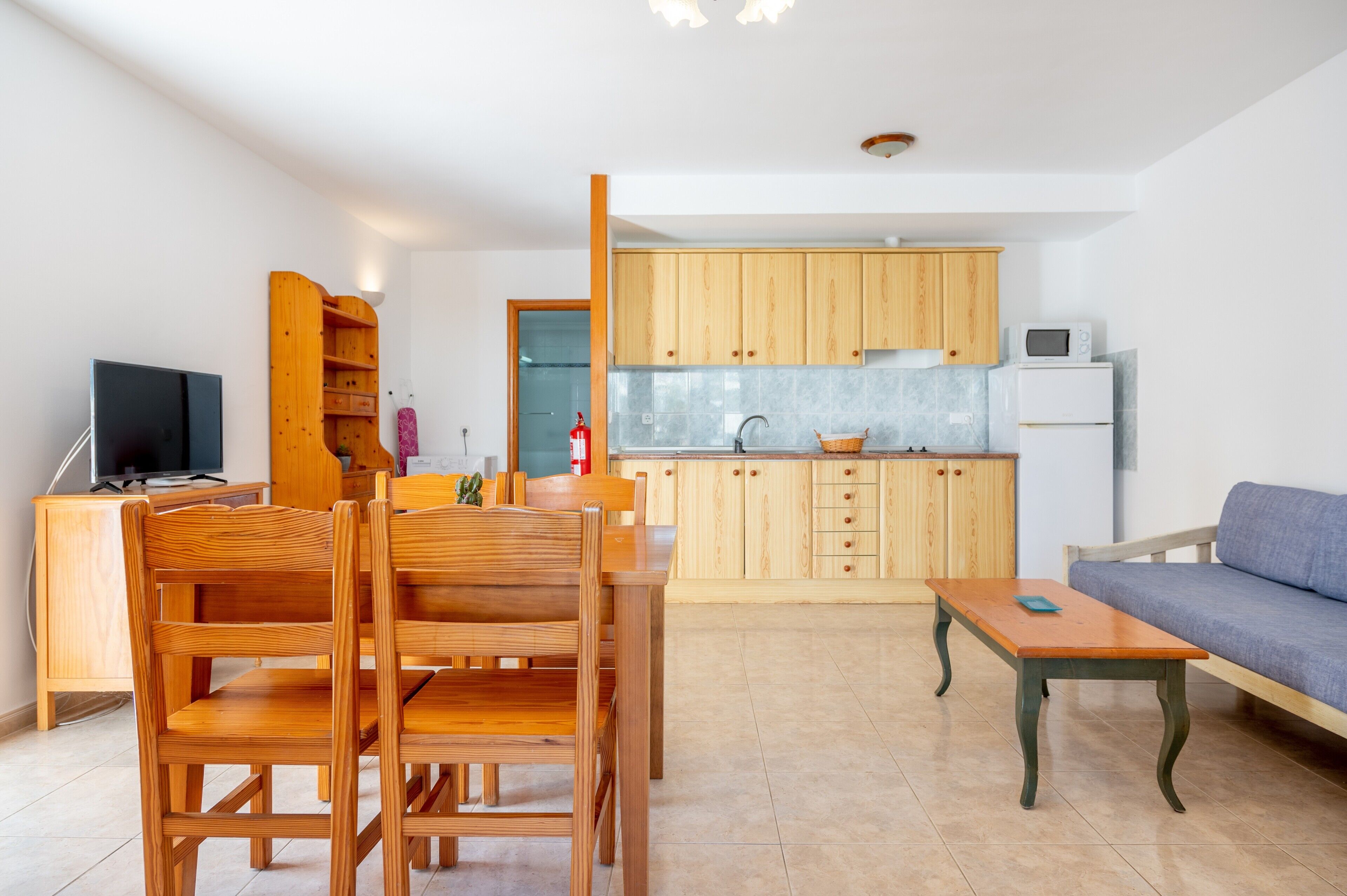 Una cocina moderna con armarios de madera, un comedor con una mesa y sillas de madera, un sofá y una televisión.