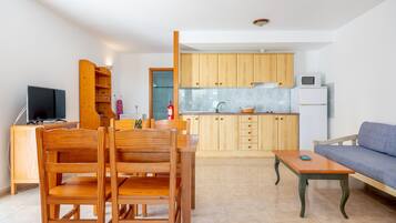 Una cocina moderna con armarios de madera, un comedor con una mesa y sillas de madera, un sofá y una televisión.
