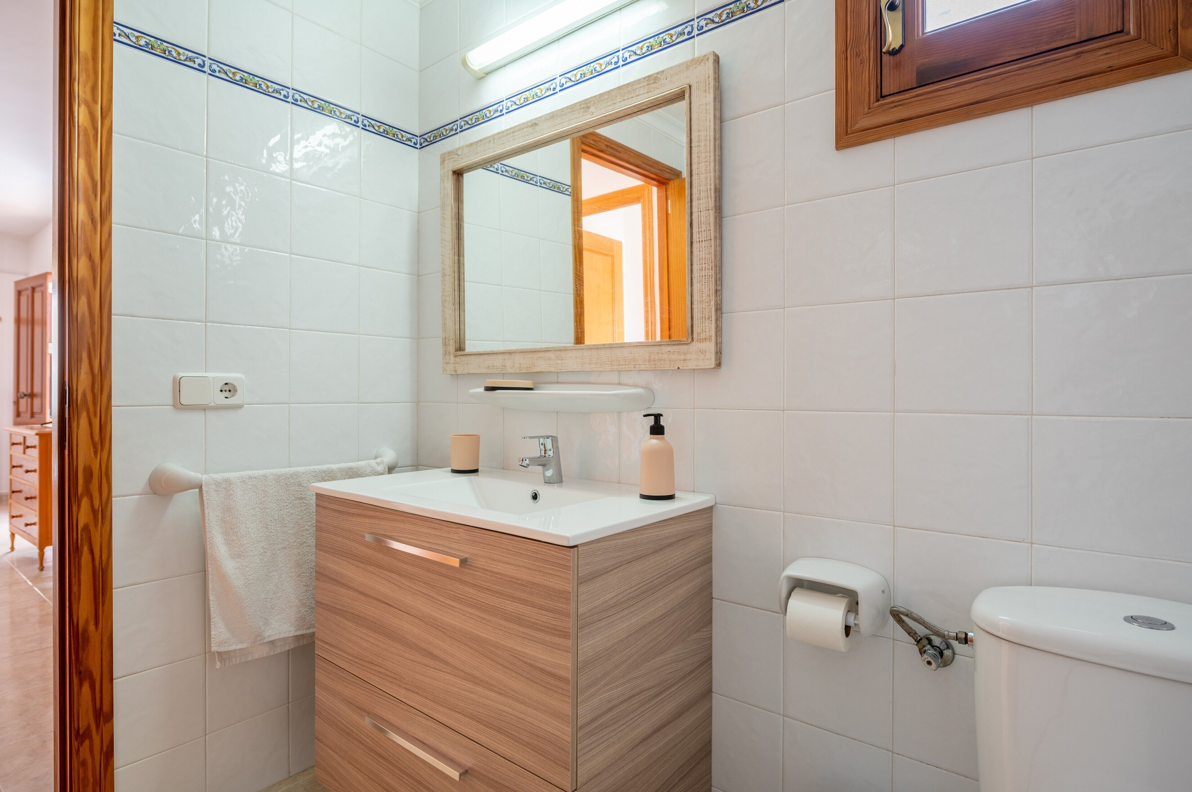 Een badkamer met een houten wastafelmeubel, een spiegel, een toilet en een handdoekhouder.