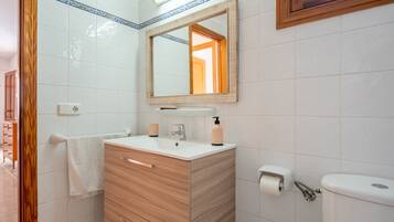Een badkamer met een houten wastafelmeubel, een spiegel, een toilet en een handdoekhouder.