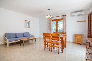 A room with a wooden dining table and chairs, a sofa, a small cabinet, and a picture on the wall.