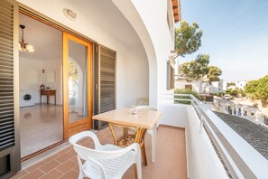 A balcony with a table and chairs, a sliding glass door leading to a room with a washing machine, and a view of the street.