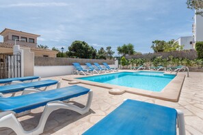 A swimming pool with sun loungers, a stone tiled deck, and a white building in the background.