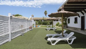 Eine Terrasse mit Kunstgrasanlage, weißen Lounge-Stühlen und einem Pool.