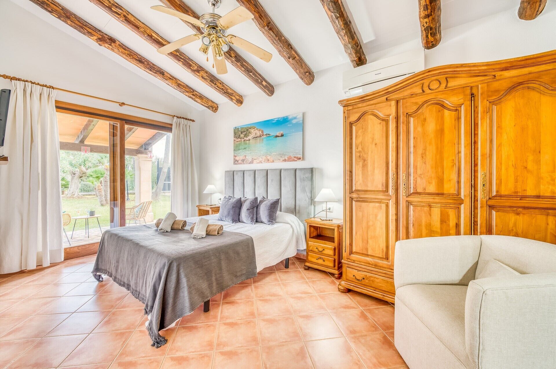 A bedroom with a bed, a nightstand, a wooden wardrobe, and a view of the outdoors.
