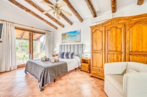 A bedroom with a bed, a nightstand, a wooden wardrobe, and a view of the outdoors.