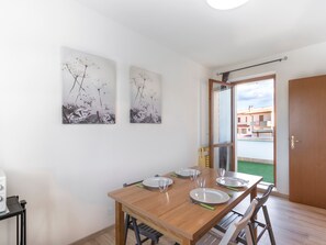 Un'area pranzo con un tavolo di legno apparecchiato per quattro persone, due opere d'arte appese alle pareti e una porta scorrevole che dà su uno spazio esterno.