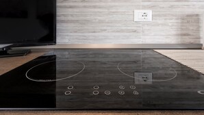 A modern kitchen with a black induction cooktop, a flat-screen TV, and a wooden backsplash. - Holiday Apartment "Bella Cora" With Garden and Private Rooftop Terrace (LAZISE)
