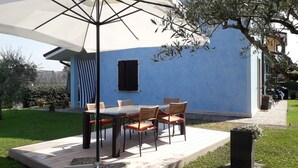 An outdoor patio with a table and chairs, a large umbrella, and a blue building in the background. - Holiday Apartment "Bella Cora" With Garden and Private Rooftop Terrace (LAZISE)