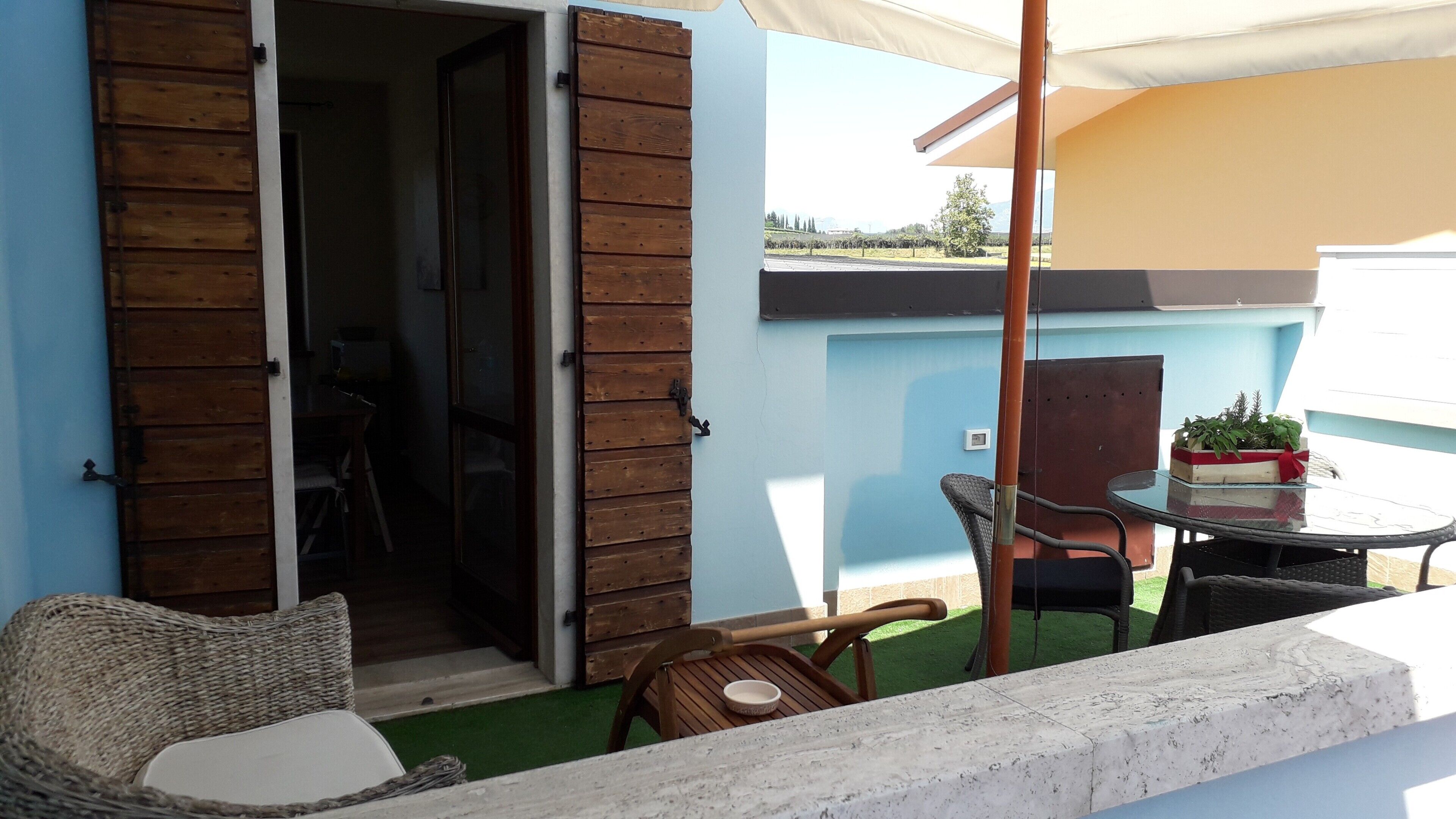 Un área de estar al aire libre con mobiliario de mimbre, una mesa con una planta en maceta y vistas del paisaje.