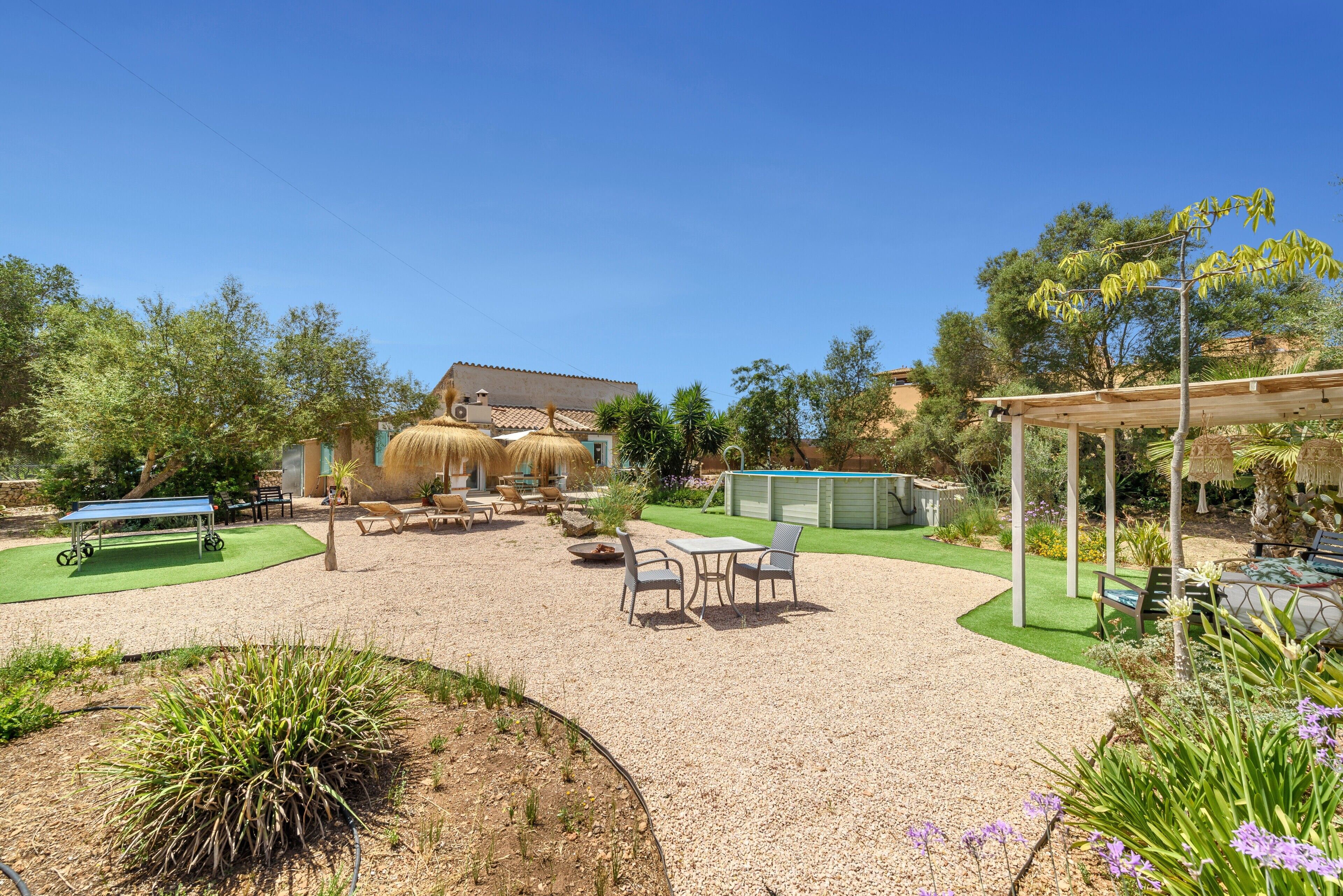 Un patio con mobiliario exterior, una pérgola y una casa al fondo.