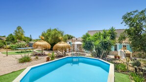 A swimming pool with a ladder, lounge chairs, and thatched umbrellas in a landscaped garden. - Can Torres. Your charming villa in the heart of Mallorca. (Pòrtol)