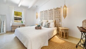 A bedroom with a large bed, a decorative headboard, a small table, and a hanging lantern. - Can Torres. Your charming villa in the heart of Mallorca. (Pòrtol)