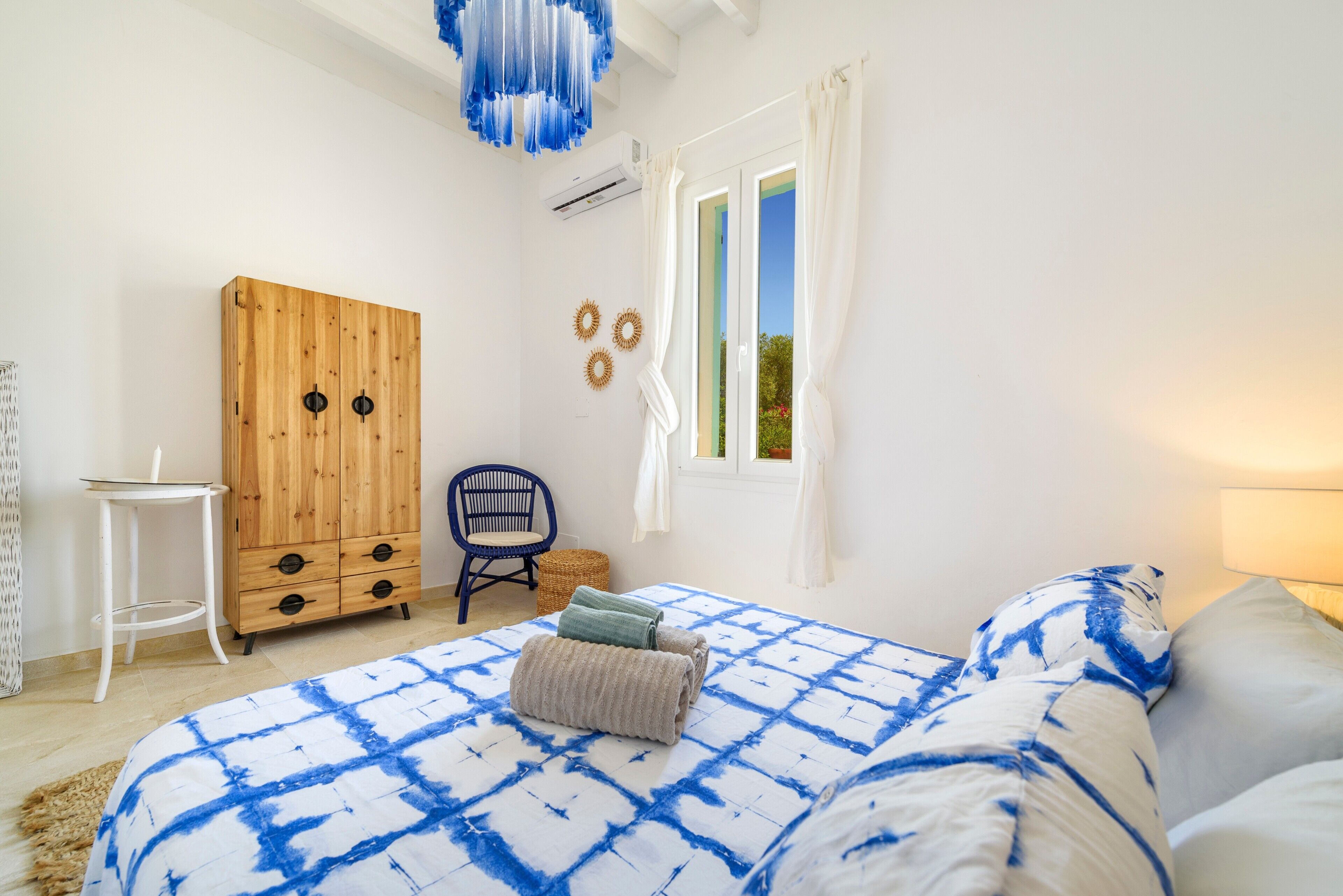 Un dormitorio con cama, armario de madera, silla, mesita y ventana con cortinas.