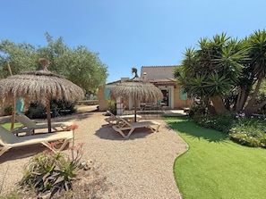 Ein Garten mit Liegestühlen, einem Reetdachschirm und einem Gebäude mit Ziegeldach.