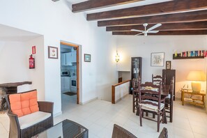 A living room with a dining area, wooden ceiling beams, a fire extinguisher, and a bookshelf.