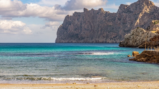 Un paisaje costero con un acantilado rocoso, mar turquesa cristalino y una playa de arena.