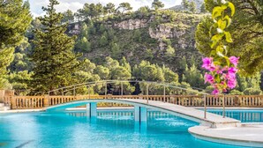 Una piscina con un puente, rodeada de árboles y un paisaje montañoso.