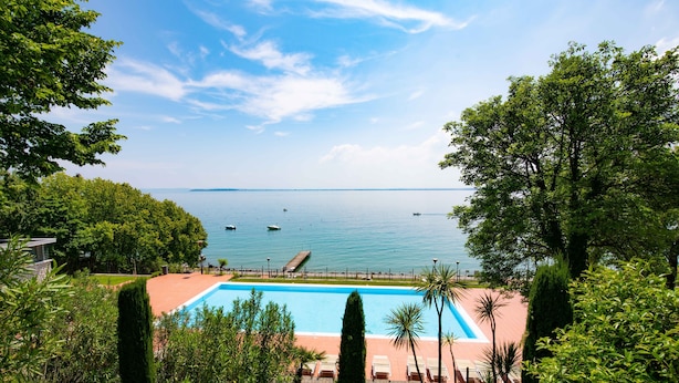 Ein Pool mit Blick auf das Meer, umgeben von Grünpflanzen und einer Holzterrasse.