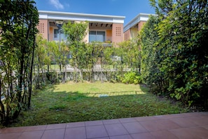 Un edificio residencial con un pequeño jardín, un balcón visible y fachada de ladrillo.