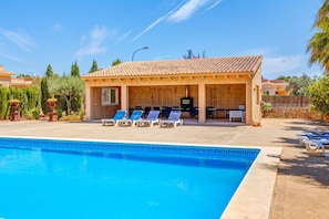 A swimming pool with lounge chairs, a covered seating area, and a stone wall.