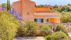 En villa i middelhavsstil med et tagdækket tag, omgivet af frodig vegetation og blomstrende planter.