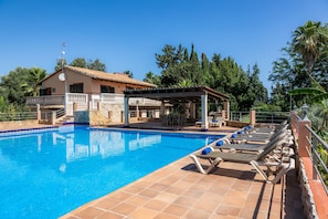 A swimming pool with lounge chairs, a covered patio, and a house with a balcony.
