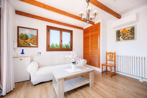 Une pièce avec un canapé blanc, une table en bois sur laquelle est posé un vase de fleurs, une chaise en bois et deux tableaux accrochés aux murs.