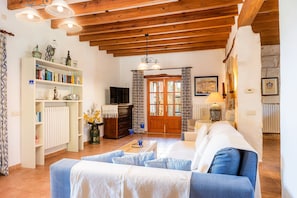 A cozy living room with a sofa, a coffee table, a bookshelf, and a television. - Country House 'Can Jener' near Muro (Llubí)