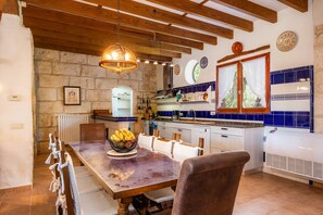 Une cuisine rustique avec un mur en pierre, des poutres en bois et une grande table à manger entourée de chaises.