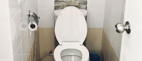 A bathroom with a toilet, a shower, and a blue trash bin.